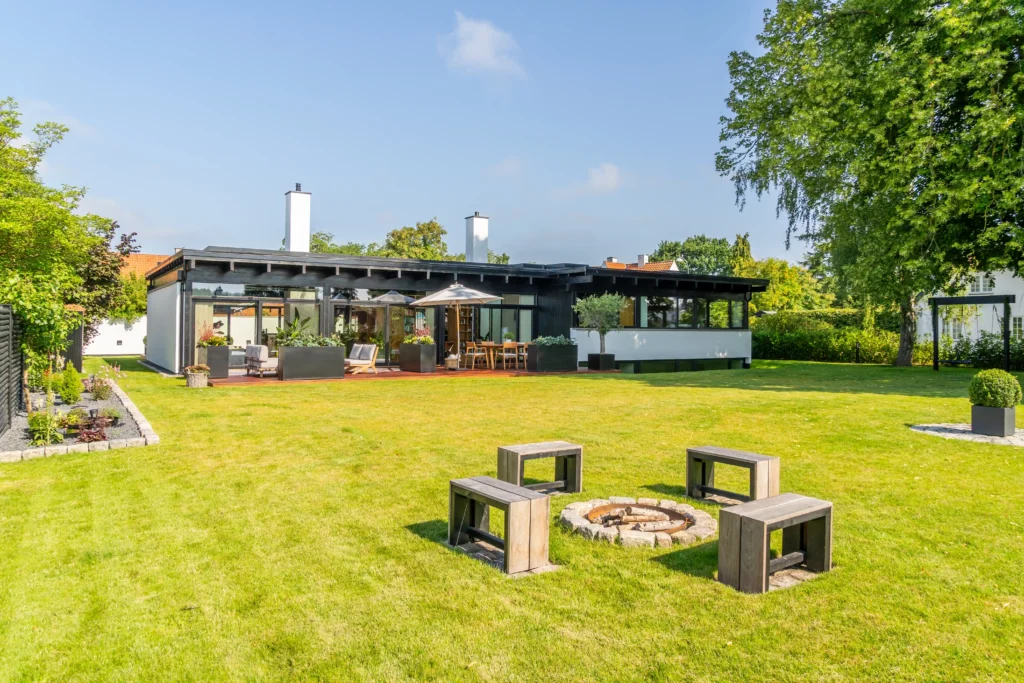 Udendørs terrasse med store hæveskydedøre i træ/alu, der integrerer haven med boligen og skaber en åben atmosfære.